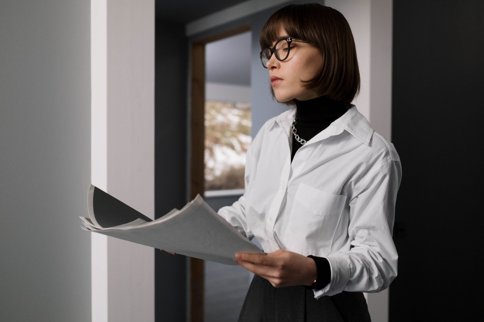Professional woman in office attire reviewing documents in an indoor setting.
