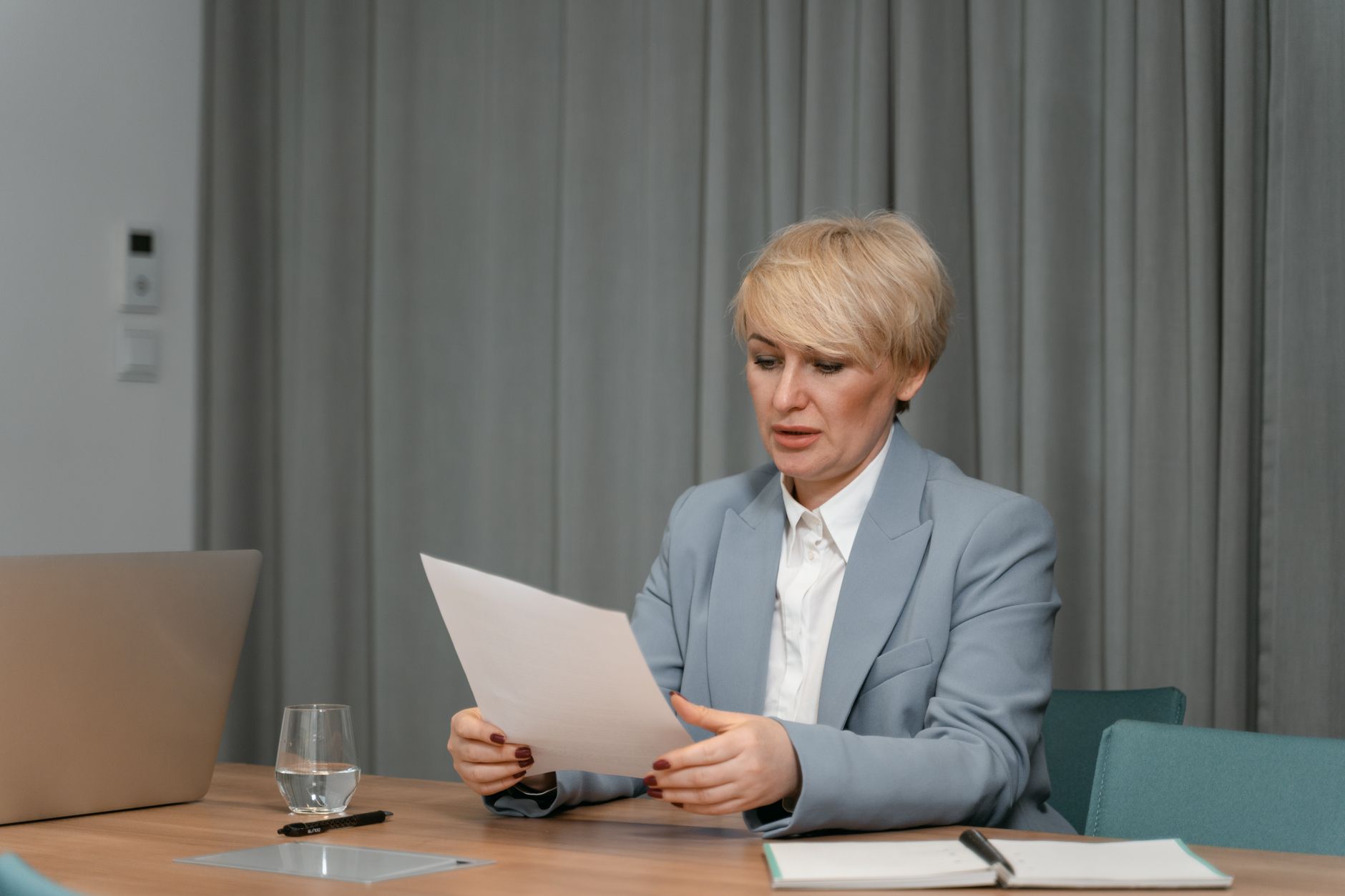 Kobieta w marynarce przegląda dokumenty przy biurku w biurze, obok laptop i papiery.